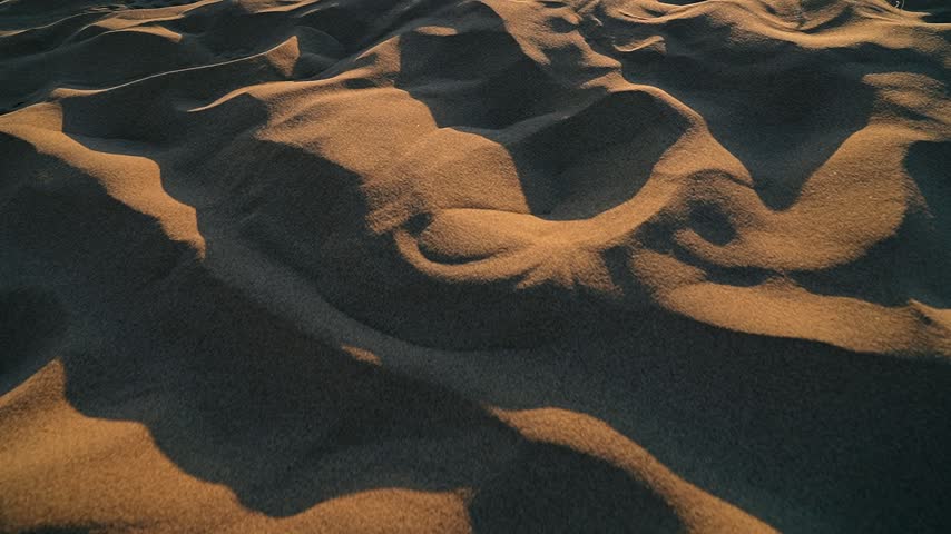Beach sand glows in yellow sunset tones in a close shot, revealing warm texture and natural detail.
