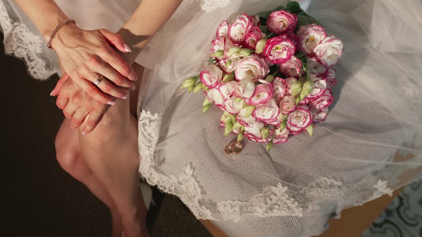 Bride sitting with a pink and white spray rose bouquet on her lace veil, close-up of hands with ring