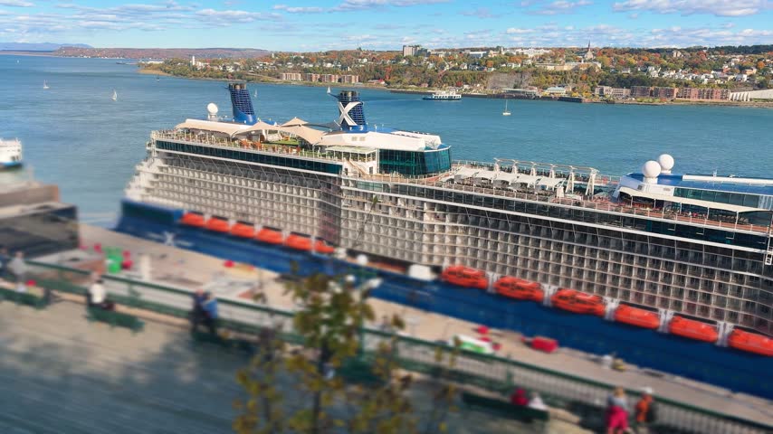 A large cruise ship docks at the port terminal in Quebec City on a sunny autumn day. High angle view showcases the massive passenger liner near the St. Lawrence River waterfront. Beautiful coastal landscape and urban scenery stretch across the background under a blue sky.