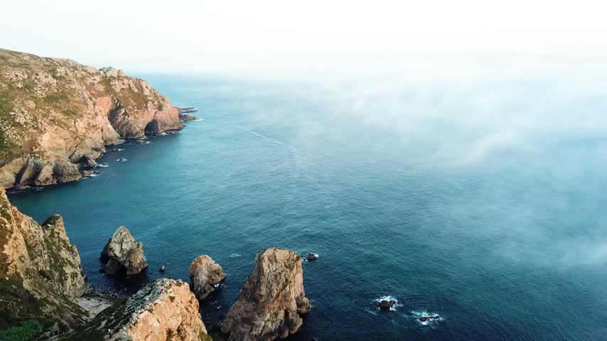 Aerial view of a rocky Portuguese cape and offshore sea stacks near Cabo da Roca, with Atlantic water beyond.