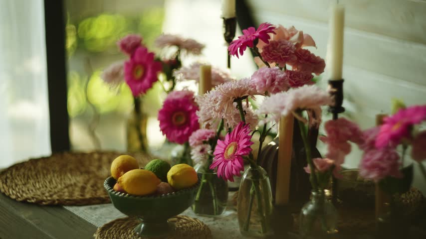 Fresh pink flowers and white candles sit near a bright window during daytime
