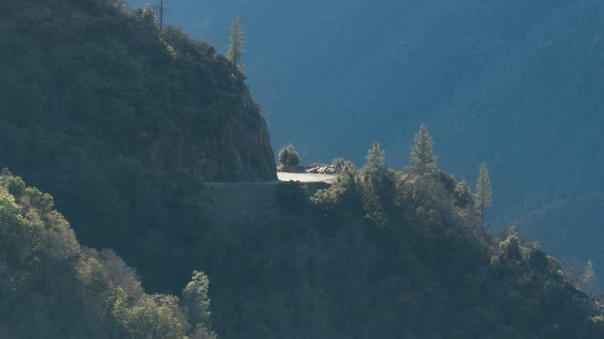 Sunlight shines on a paved mountain pass carved into steep forest terrain