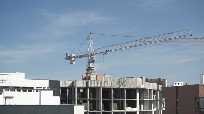 A short video capturing a massive construction crane slowly rotating above an unfinished multi-story building
