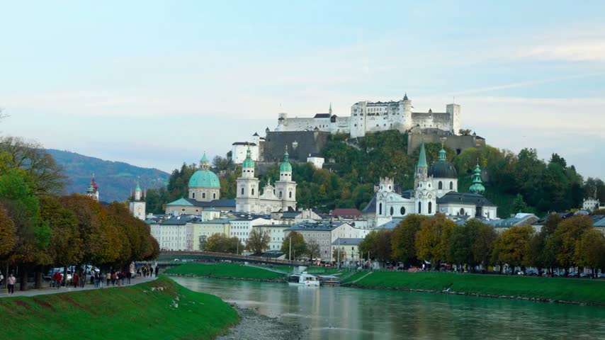 Panoramic view of Hohensalzburg Fortress in Salzburg, Austria, at dusk, showcasing the historic hilltop castle, church architecture, and charming city skyline in atmospheric evening light.