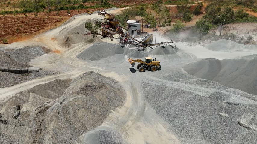 Yellow loader moving gravel piles at a busy stone quarry facility in South Kalimantan