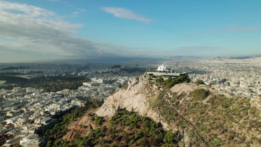 Aerial panorama of Athens, Greece, featuring Lycabettus Hill Park in the foreground and an expansive city skyline with dense buildings under daylight.