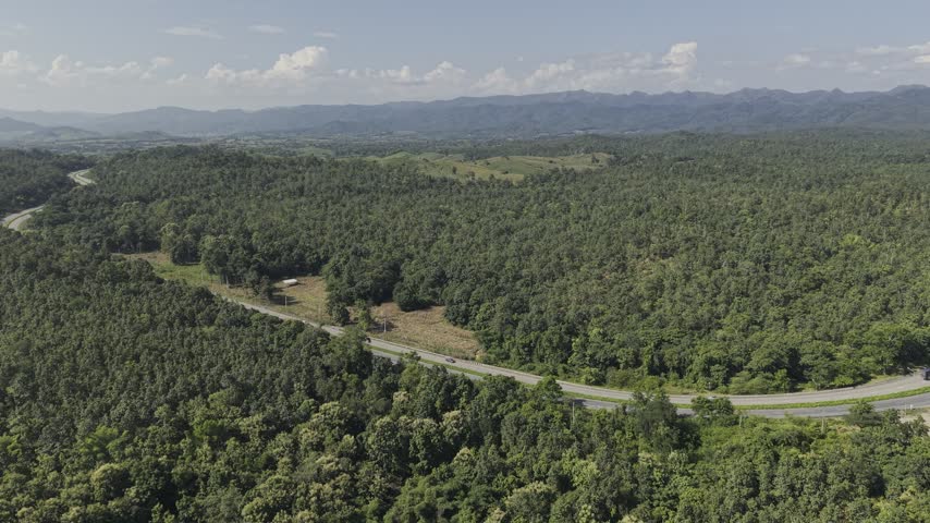 Beautiful aerial perspective of a forested mountain valley with a scenic highway and sunlit cloudscape.