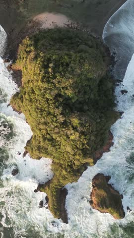 Aerial view pulling away from a small tropical island surrounded by rough turquoise ocean waves crashing against the rocky coastline. Dramatic cinematic reveal shot showing the vast open sea and stunning natural landscape from high altitude.