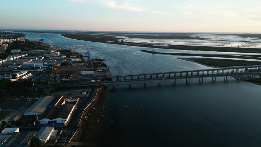 Aerial drone shot gliding forward over the industrial port of Huelva Spain at twilight with a river bridge and towering cranes beside marshes in a global trade and logistics supply chain concept.
