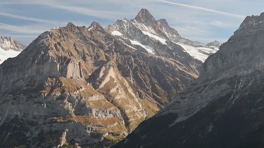 Sunlight falls across rugged mountain ridges and lingering snowfields near Grindelwald beneath a clear blue autumn sky.