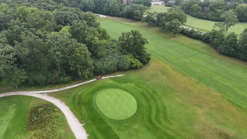 Aerial flyover of tree canopy and a putting green beside a curving cart path on a golf course. Filmed in River Grove, Illinois.
