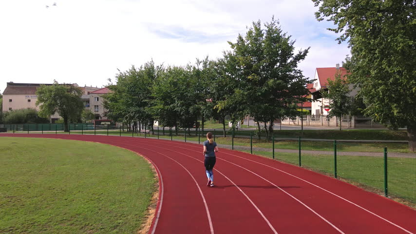 Woman runs on a red track at an outdoor stadium. Female runner training on an athletics track. Jogging, fitness, exercise and active lifestyle.