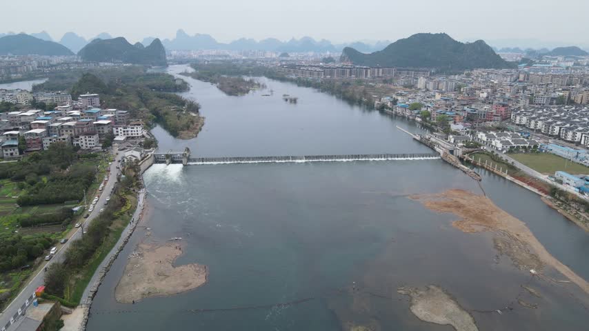 Aerial view of a wide river dam with flowing water and surrounding urban city