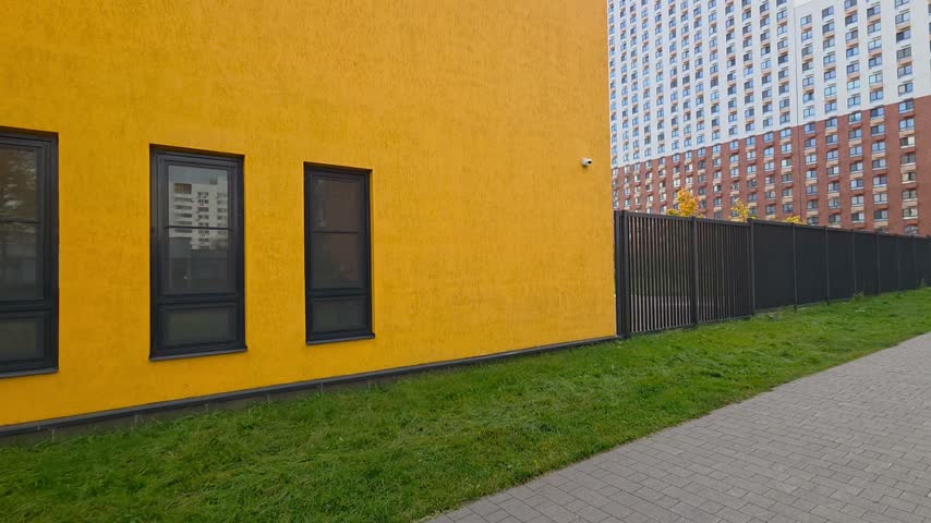 Yellow facade, dark windows, modern architecture, geometric pattern, green lawn. Bright ochre building wall with five evenly spaced rectangular windows and minimalist urban design