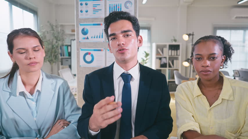 Three professional colleagues looking at a camera together, discussing project details during an online video conference with a client.