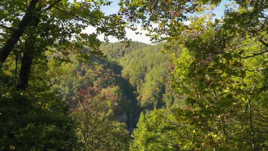 A view through lush autumn foliage of mountains and a waterfall. Autumn landscape.
