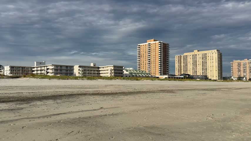 Pan view of tall and buildings and short motels along the shoreline by the beach. The skyline of Atlantic city is also scene