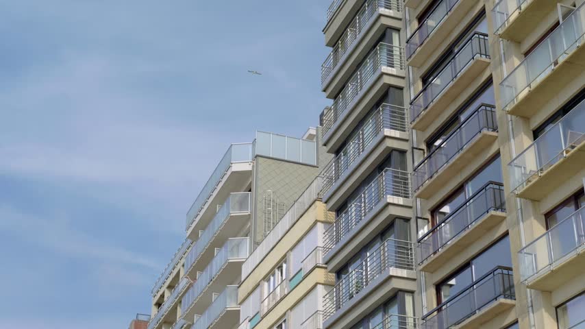 Seagulls fly over high rise houses with balconies slow motion a blue sky in the background