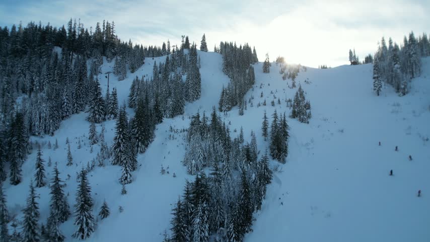 Winter aerial skiing from above snow-filled slopes with skiers and chairlifts in the Pacific Northwest