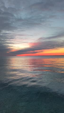 Vibrant sunrise over the ocean water with calm waves and colourful clouds in the sky.