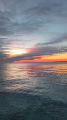 A tranquil sunrise over calm ocean waters with vibrant colors reflecting across the surface.