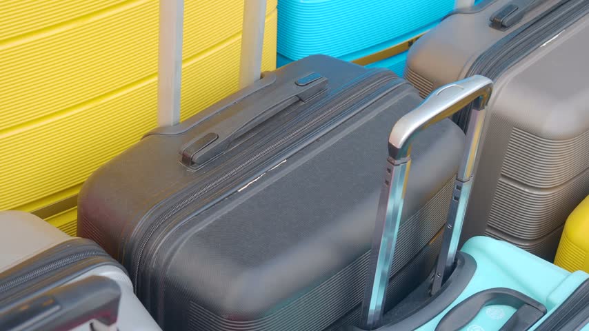 High angle shot of stacked travel luggage in various colors including yellow black gray and blue for vacation preparation or tourism concepts with rolling wheels and telescopic handles.