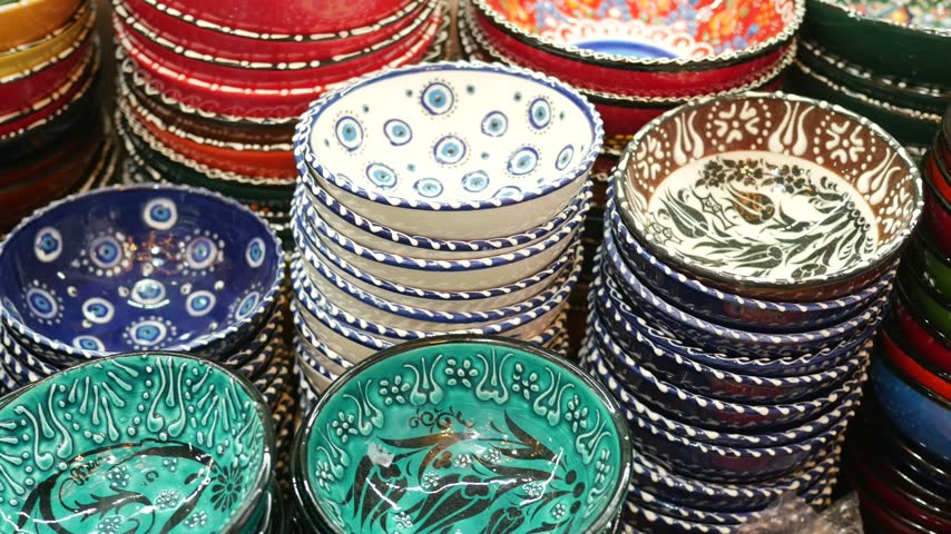 Close up view of stacks of vibrant ceramic bowls featuring intricate traditional patterns and eye motifs at turkish bazaar. Handcrafted pottery collection for kitchen home decor.