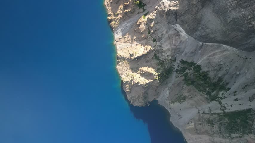 Artistic cinematic top-down aerial drone view of Crater Lake National Park, Oregon, revealing the dramatic contrast between deep blue volcanic water and rugged crater cliffs under sunlight