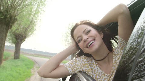 Young woman sitting in car passenger seat looking out window on sunny day with flare 