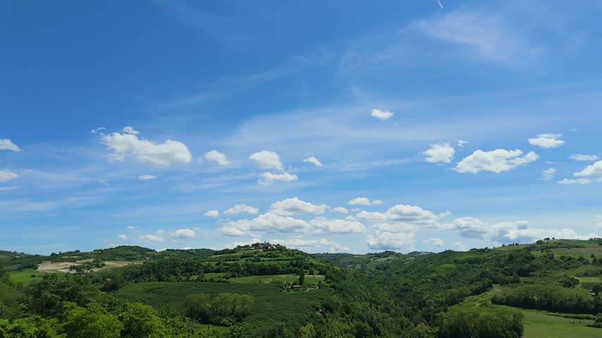 White fluffy clouds drift across a blue sky over green rolling hills in Piedmont.