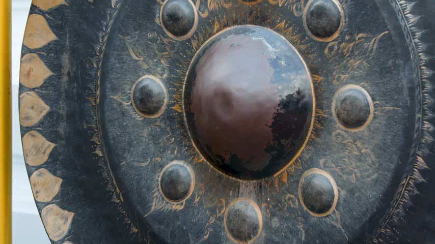 A visitor strikes a large bronze Buddhist gong with a padded mallet in Bangkok, Thailand.