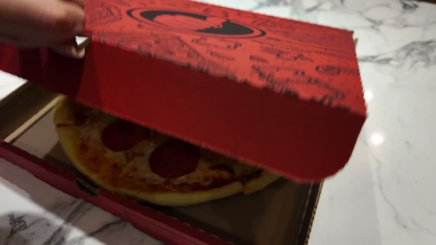 Freshly baked pepperoni pizza sitting inside an open cardboard box on a marble table. Hot takeaway meal with melted cheese and salami
