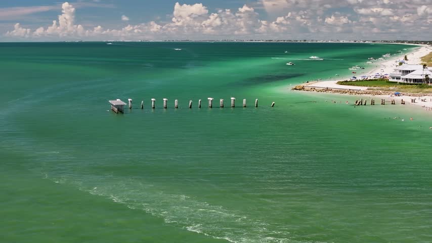A cinematic, low-flying 70mm drone shot, slowly rotating around the scenic barrier-island coastline and turquoise Gulf waters, near Gasparilla Island State Park and Boca Grande, Florida.