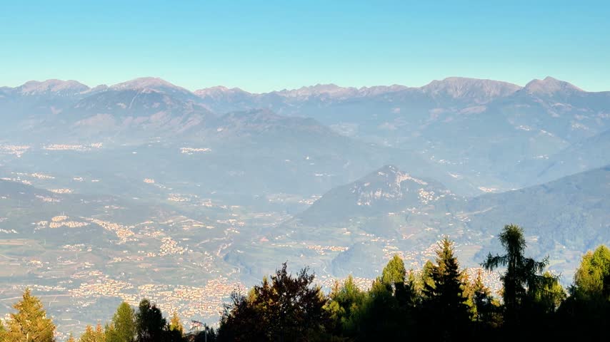 Mountain panorama overlooking treetop peaks under a blue sky seen from Monte Bondone in Trentino, Northern Italy