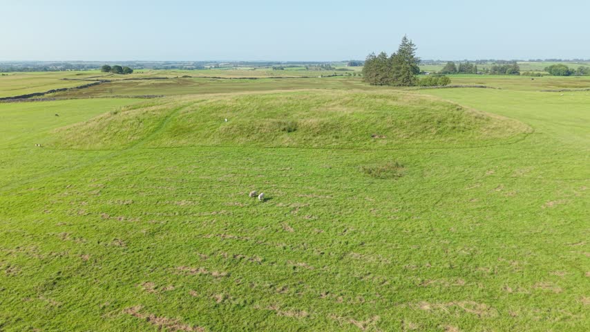 Wide aerial view of grassy Rathcroghan Mound in open rural landscape, sunny day