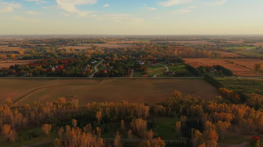 Detached houses line winding roads amid autumn trees and broad lawns, with cultivated fields, ponds and power lines surrounding the neighborhood in northern Wisconsin