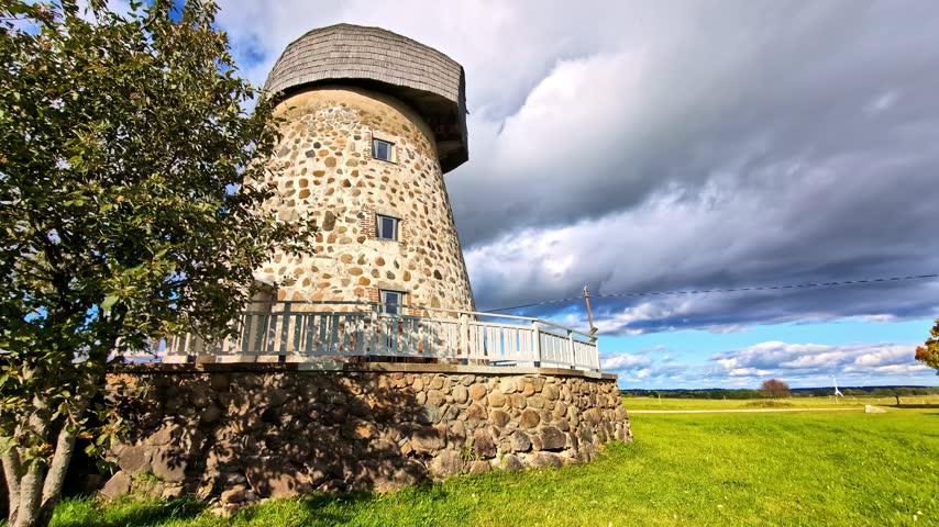 Historic stone windmill on a rural agricultural meadow with dramatic cloudy sky moving in summer
