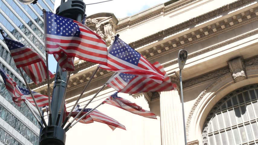 American flags near Grand Central Terminal on 42 street, New York City, Manhattan Midtown. Railway building architecture in United States. Public railroad transport junction. Old station exterior.