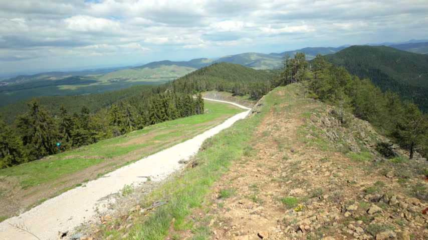 Mountain Ridge Trail Leads Toward Wooden Viewing Bridge. A camera sweeps across a highland path and timber span beneath drifting clouds
