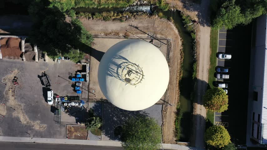 Top-down aerial drone view of a white water tower beside a road, parking lot and dry lots in Meridian, Idaho.