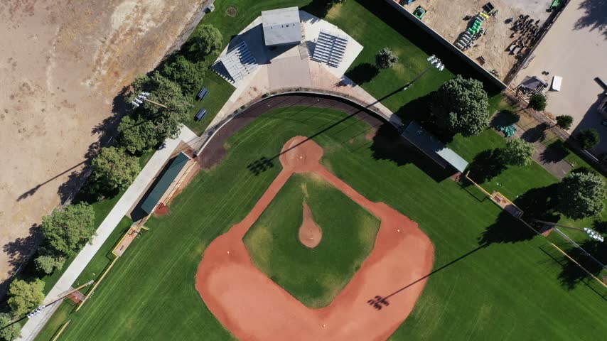 Top-down aerial drone view of a small baseball diamond with dugouts and a parking lot beside it in Meridian, Idaho.