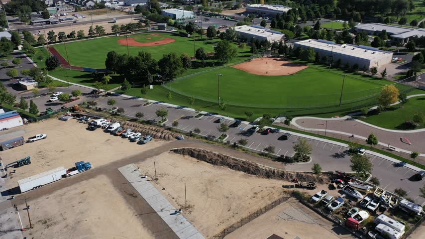 Aerial drone view over baseball diamonds, a parking lot and town buildings in Meridian, Idaho, with hills beyond.