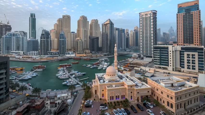 Aerial-style wide view of Dubai Marina, UAE, featuring modern high-rise skyscrapers, luxury waterfront residences, yachts and boats along the marina canal, and a beautiful mosque in the foreground. Urban architecture, waterfront development, tourism, and modern Middle Eastern city life.