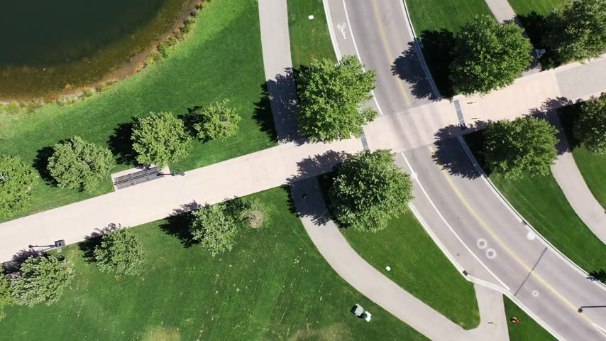 Top-down aerial drone view of a winding path between two green ponds with a fountain in a Meridian, Idaho park.