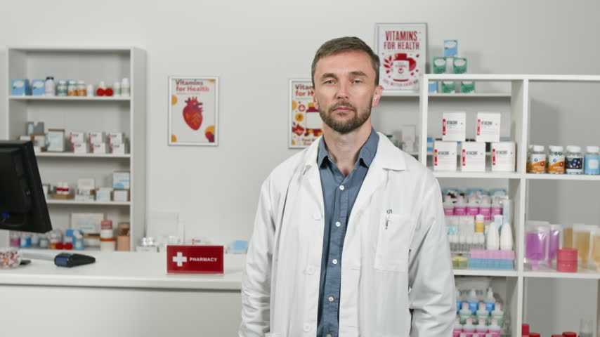 Portrait of middle aged Caucasian male pharmacist crossing arms and looking at camera in pharmacy store. Clip suitable for healthcare advertising, medical training, and pharmaceutical promos