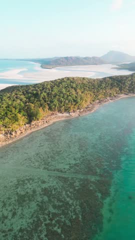 Aerial view of the Whitsundays coastline with turquoise waters, coral reefs, and lush green hills in Whitsundays, Queensland, Australia.