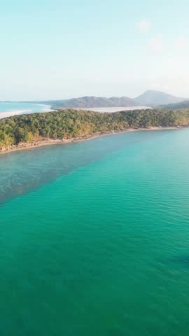 Aerial view of the turquoise waters and lush green coastline of the Whitsundays, Queensland, Australia.