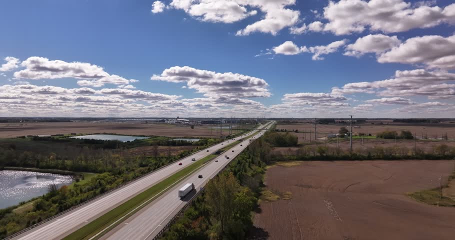 Aerial view of a highway with vehicles driving through rural fields under a blue sky with scattered clouds in Washington Court House, Ohio, United States.