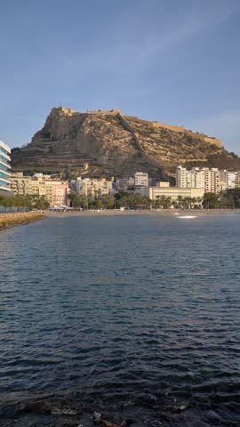 Vertical shot of a calm sea at morning with Postiguet beach and Santa Barbara Castle on the background. Sunrise light over Alicante coast in Spain.