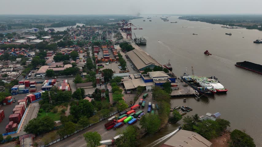 Aerial view of busy port with shipping containers and cargo ships along the river in Indonesia.
